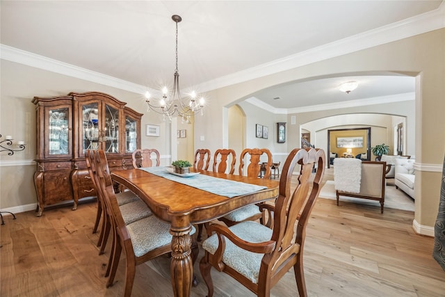 dining space featuring an inviting chandelier, ornamental molding, baseboards, arched walkways, and light wood finished floors