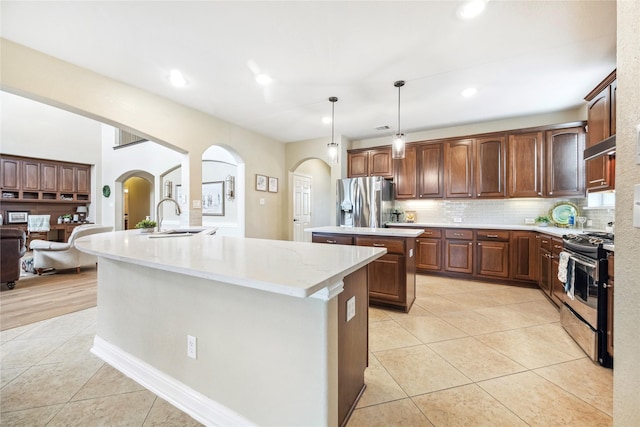 kitchen featuring a center island with sink, appliances with stainless steel finishes, pendant lighting, a sink, and light tile patterned flooring