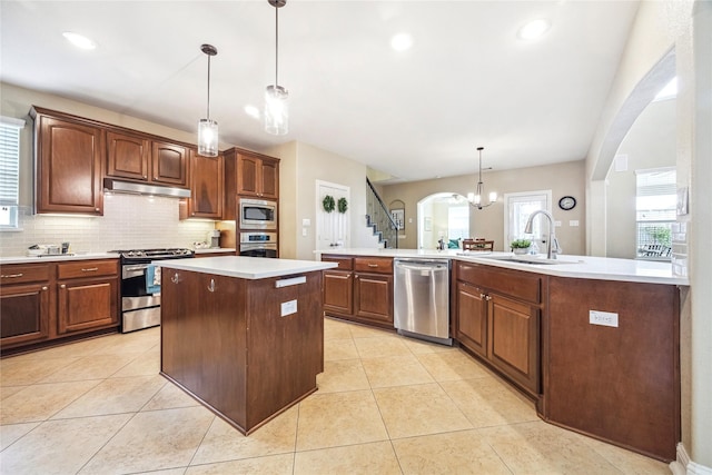 kitchen featuring arched walkways, an island with sink, appliances with stainless steel finishes, light countertops, and a sink