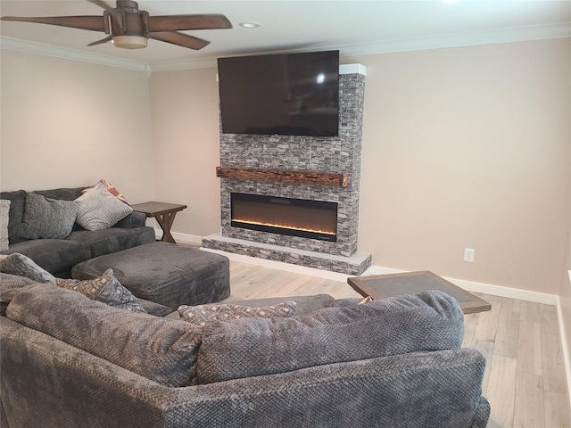 living room featuring ornamental molding, a stone fireplace, ceiling fan, and light wood-type flooring