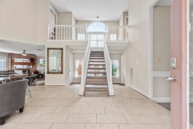 tiled foyer entrance with a high ceiling, plenty of natural light, a fireplace, and ceiling fan