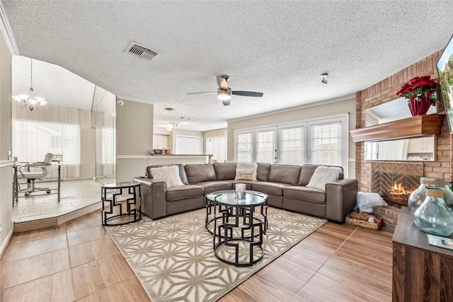 living room featuring a brick fireplace, ceiling fan with notable chandelier, and a textured ceiling