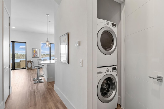 clothes washing area featuring hardwood / wood-style flooring and stacked washer and clothes dryer