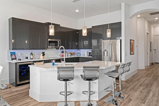 kitchen featuring a kitchen island with sink, stainless steel appliances, a kitchen bar, decorative light fixtures, and beverage cooler