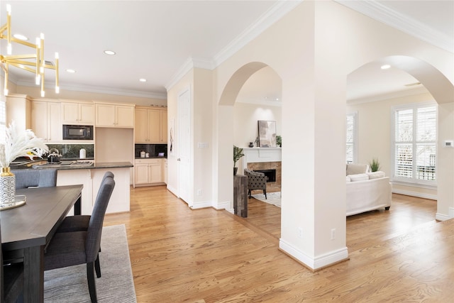 kitchen with a breakfast bar area, crown molding, tasteful backsplash, black microwave, and light hardwood / wood-style floors