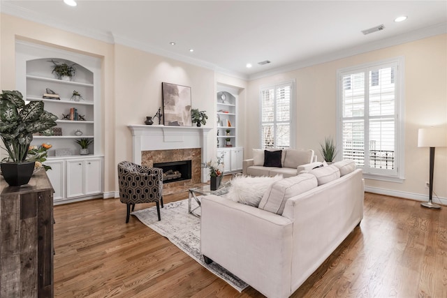 living room with hardwood / wood-style floors, built in shelves, a fireplace, and ornamental molding