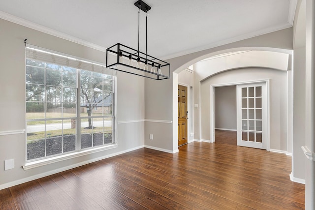 unfurnished dining area featuring arched walkways, ornamental molding, wood finished floors, a chandelier, and baseboards