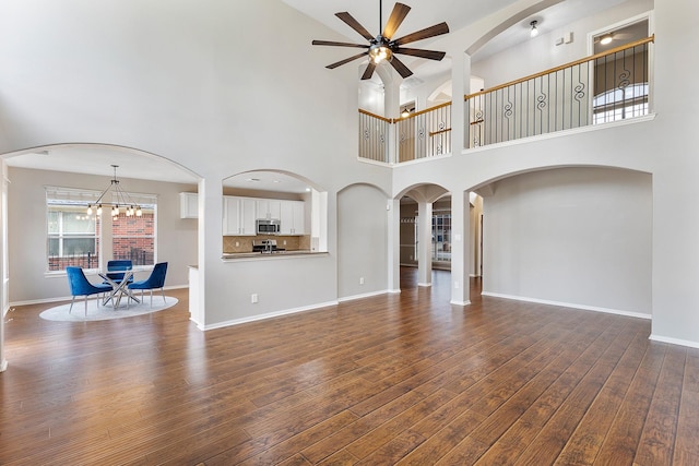 unfurnished living room with ceiling fan with notable chandelier, arched walkways, dark wood finished floors, and baseboards