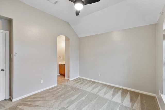 unfurnished bedroom featuring arched walkways, light colored carpet, vaulted ceiling, ensuite bath, and baseboards