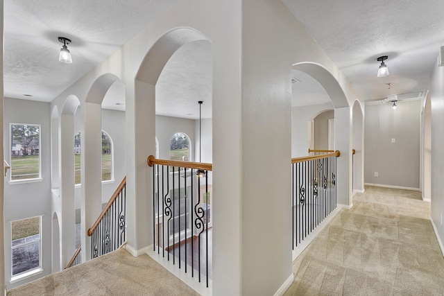 corridor with light carpet, a wealth of natural light, and a textured ceiling