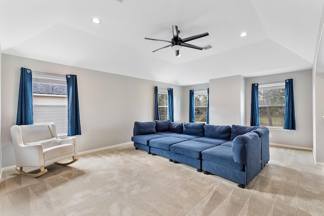 living area featuring a ceiling fan, a tray ceiling, light carpet, and baseboards