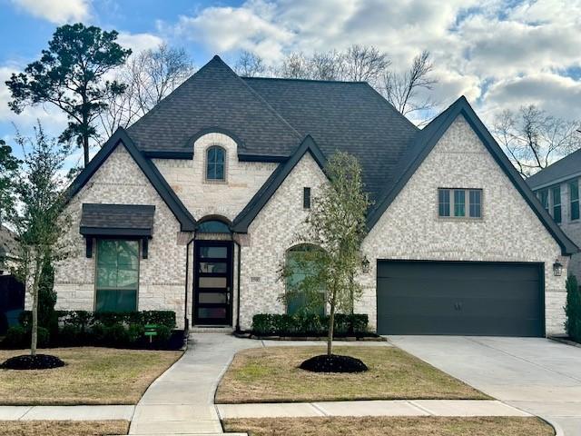 11910 Gramina Way, Humble, TX 77346 - french country home featuring driveway, a front lawn, stone siding, and roof with shingles