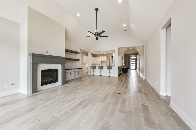 unfurnished living room with ceiling fan, a stone fireplace, and high vaulted ceiling