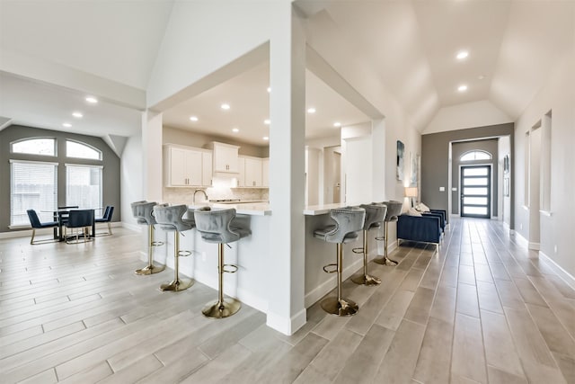 kitchen with kitchen peninsula, vaulted ceiling, a breakfast bar, and white cabinets