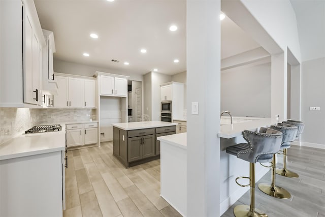 kitchen featuring white cabinetry, backsplash, gray cabinetry, and a breakfast bar