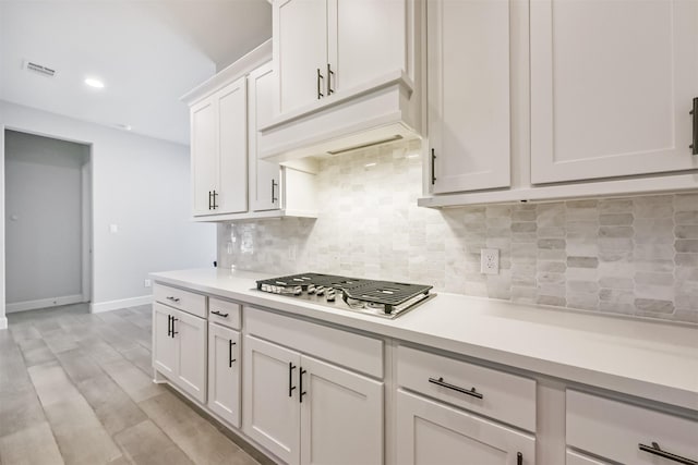 kitchen with stainless steel gas stovetop, white cabinets, light wood-type flooring, and decorative backsplash