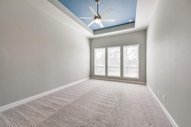 empty room with a tray ceiling, light colored carpet, and ceiling fan