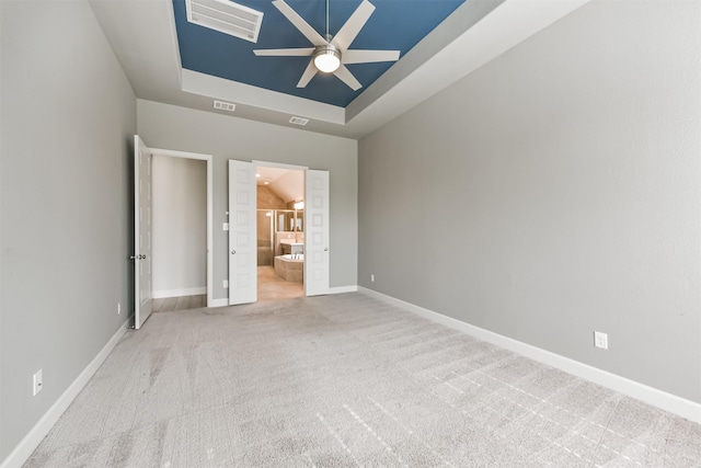 unfurnished bedroom with ensuite bath, light colored carpet, a raised ceiling, and ceiling fan