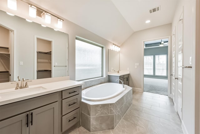 bathroom with lofted ceiling, ceiling fan, tile patterned flooring, vanity, and a relaxing tiled tub