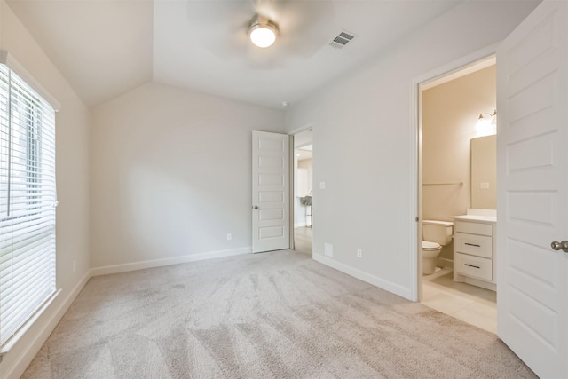 unfurnished bedroom featuring ceiling fan, light colored carpet, ensuite bathroom, and vaulted ceiling