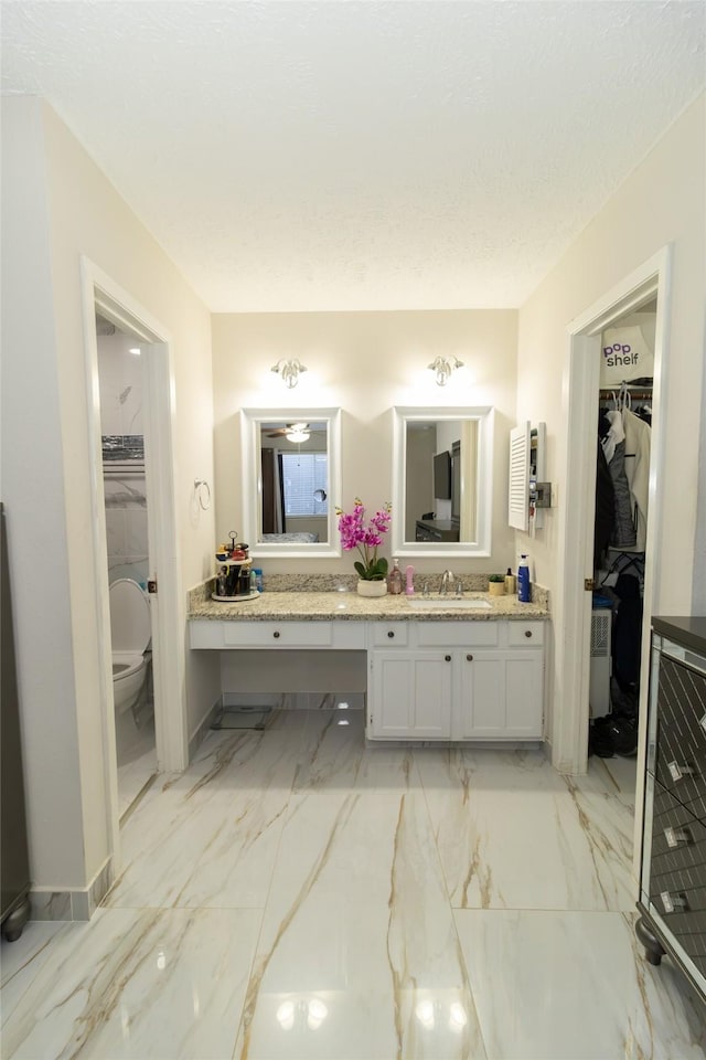 full bathroom featuring a walk in closet, toilet, marble finish floor, a textured ceiling, and vanity