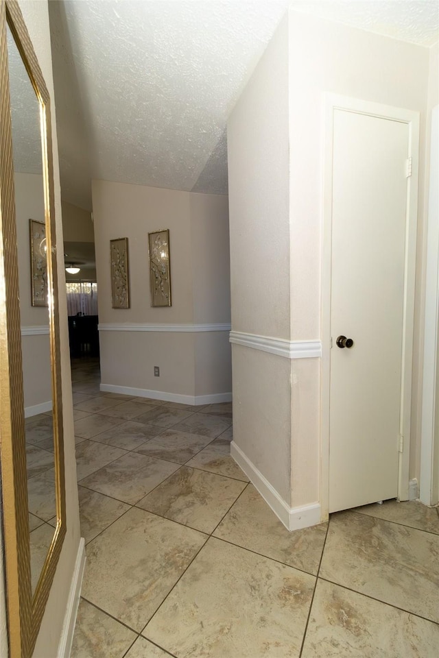 corridor with baseboards, lofted ceiling, and a textured ceiling