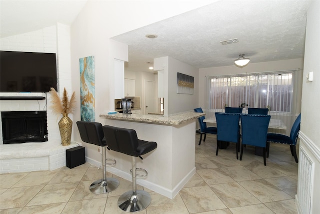 kitchen with light stone counters, a fireplace, a textured ceiling, white cabinets, and kitchen peninsula