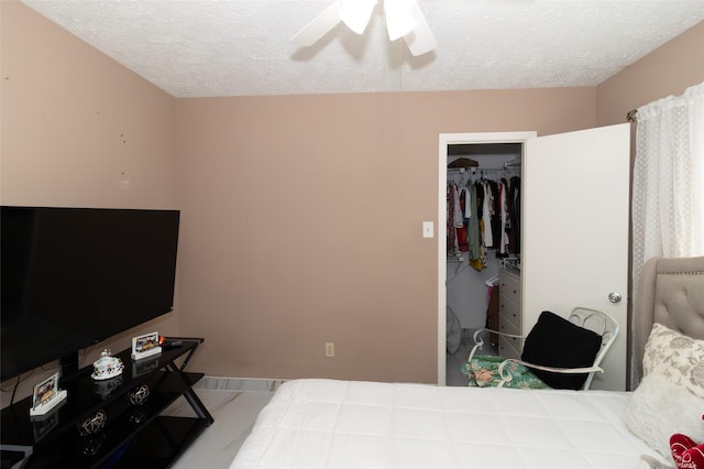 bedroom with ceiling fan, a textured ceiling, and a walk in closet