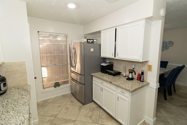 kitchen with a textured ceiling, white cabinetry, stainless steel fridge with ice dispenser, light tile patterned floors, and light stone countertops