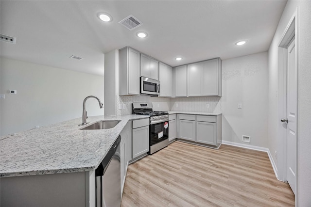 kitchen with sink, appliances with stainless steel finishes, kitchen peninsula, light stone countertops, and light hardwood / wood-style floors