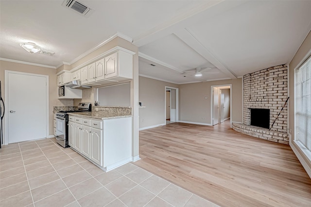 kitchen featuring stainless steel stove, white cabinetry, ceiling fan, crown molding, and a brick fireplace