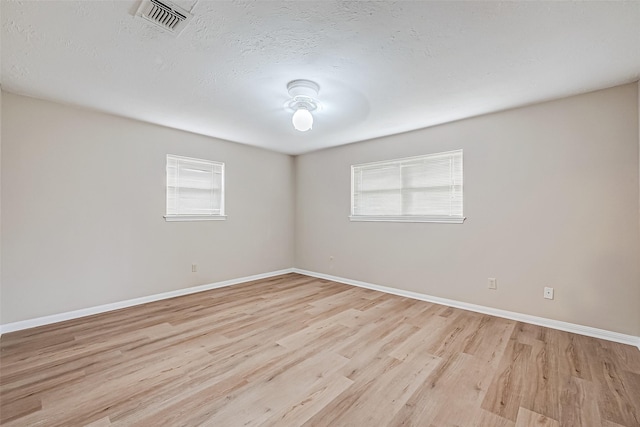 spare room featuring plenty of natural light, a textured ceiling, and light hardwood / wood-style floors