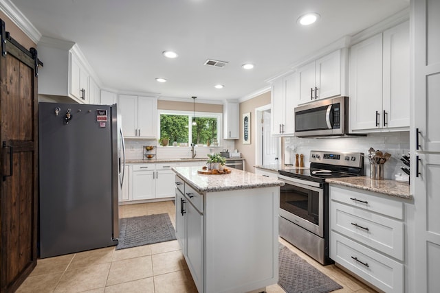 kitchen featuring sink, hanging light fixtures, appliances with stainless steel finishes, a barn door, and white cabinets