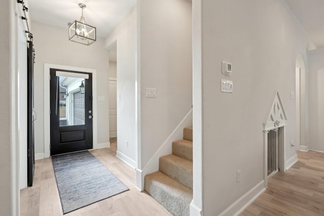 foyer entrance featuring a barn door, a notable chandelier, and light hardwood / wood-style floors