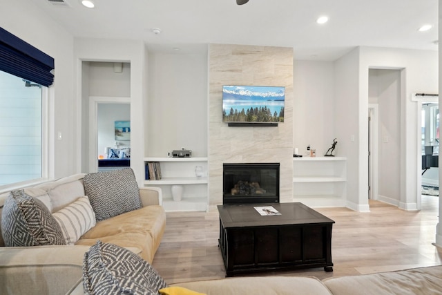 living room featuring a tiled fireplace, light hardwood / wood-style floors, and a healthy amount of sunlight