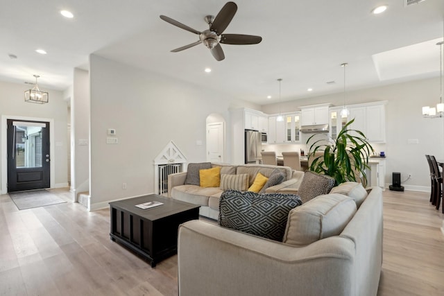 living room featuring ceiling fan with notable chandelier and light wood-type flooring