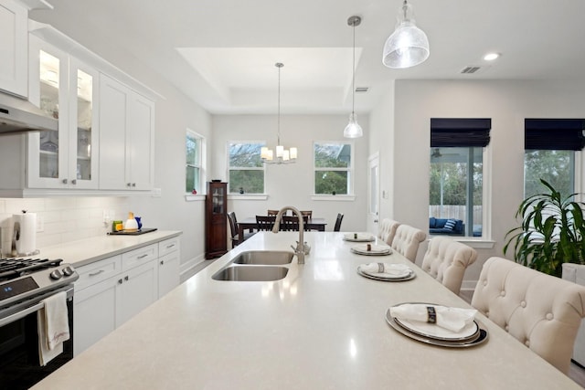 kitchen featuring white cabinetry, stainless steel range with gas cooktop, sink, and decorative light fixtures