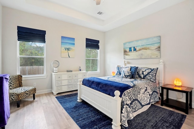 bedroom with hardwood / wood-style flooring, a tray ceiling, and multiple windows