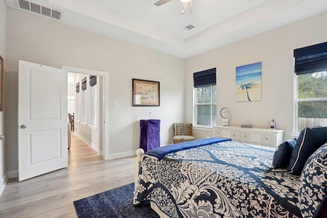 bedroom featuring multiple windows, a raised ceiling, ceiling fan, and light hardwood / wood-style floors