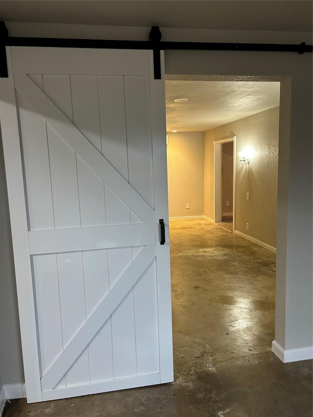 hallway with concrete flooring, a barn door, and a textured ceiling