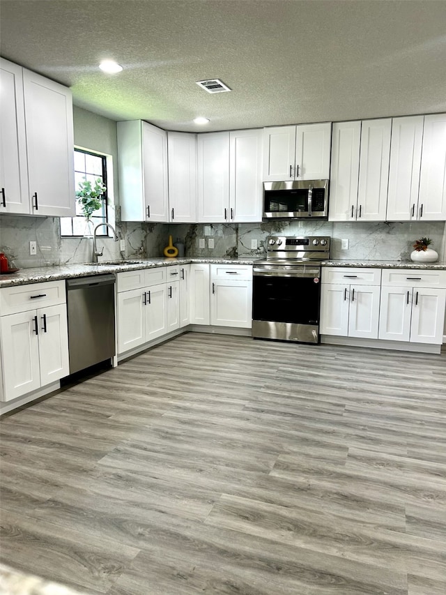 231 Dehart St Unit Cr653, Liverpool, TX 77577 - kitchen featuring stainless steel appliances, white cabinetry, decorative backsplash, light wood-style flooring, and a textured ceiling