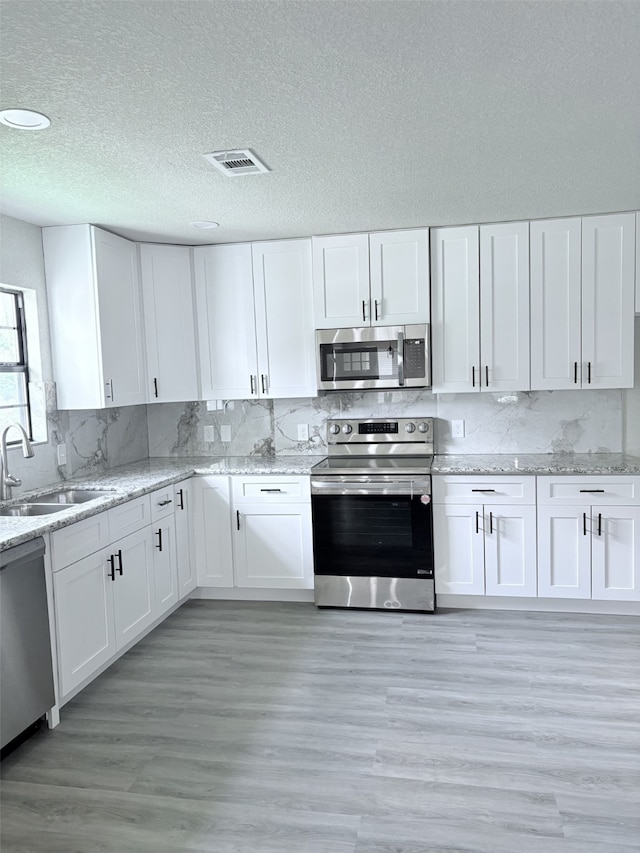 231 Dehart St Unit Cr653, Liverpool, TX 77577 - kitchen with stainless steel appliances, white cabinetry, a textured ceiling, tasteful backsplash, and light stone countertops