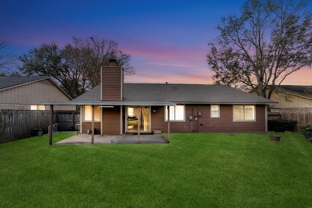 back house at dusk with a lawn and a patio