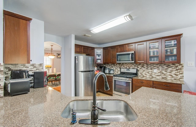 kitchen featuring sink, hanging light fixtures, appliances with stainless steel finishes, light stone countertops, and decorative backsplash