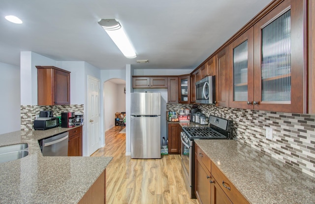 kitchen with sink, light stone counters, light wood-type flooring, appliances with stainless steel finishes, and backsplash