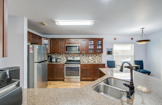 kitchen with sink, tasteful backsplash, light stone counters, hanging light fixtures, and stainless steel appliances