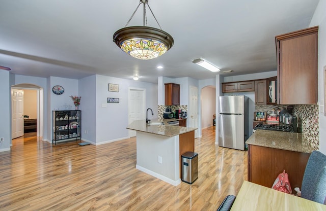 kitchen with pendant lighting, light hardwood / wood-style flooring, light stone countertops, and appliances with stainless steel finishes