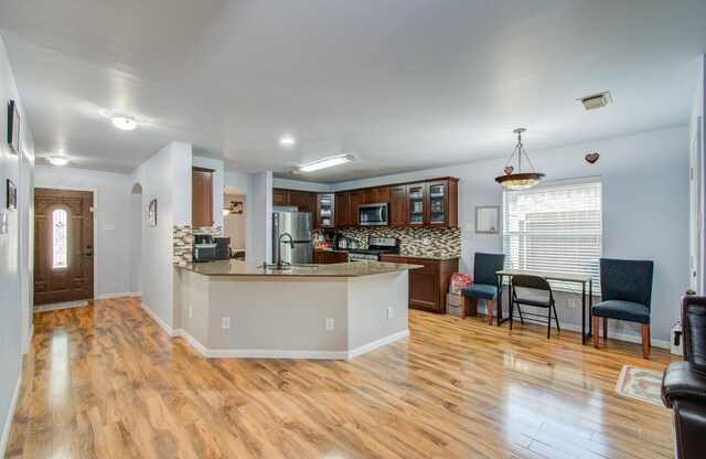 kitchen with appliances with stainless steel finishes, decorative light fixtures, tasteful backsplash, kitchen peninsula, and light hardwood / wood-style flooring