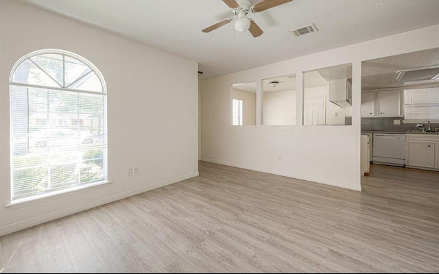 unfurnished living room with baseboards, visible vents, light wood-style flooring, ceiling fan, and a sink