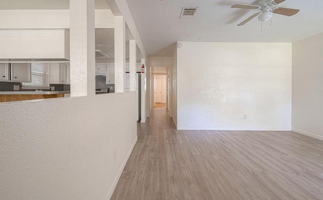 unfurnished living room with light wood-style floors, visible vents, ceiling fan, and baseboards